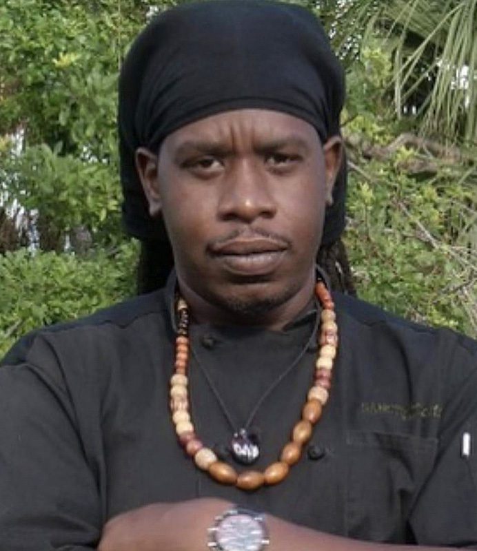 A man with dreadlocks wearing an apron and necklace.